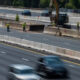 Highway construction zone with workers in reflective vests, concrete barriers, and an excavator at work near a split in traffic.