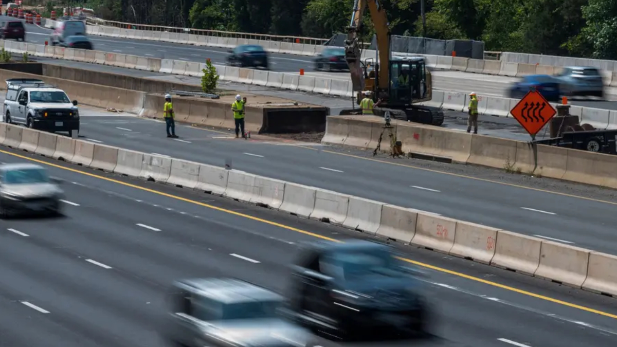 Highway construction zone with workers in reflective vests, concrete barriers, and an excavator at work near a split in traffic.