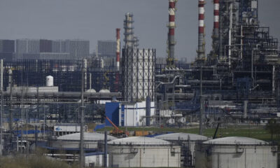 Extensive chemical refinery complex with storage tanks, pipes, and tall red-and-white smokestacks.