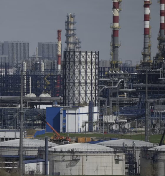 Extensive chemical refinery complex with storage tanks, pipes, and tall red-and-white smokestacks.