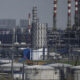 Extensive chemical refinery complex with storage tanks, pipes, and tall red-and-white smokestacks.