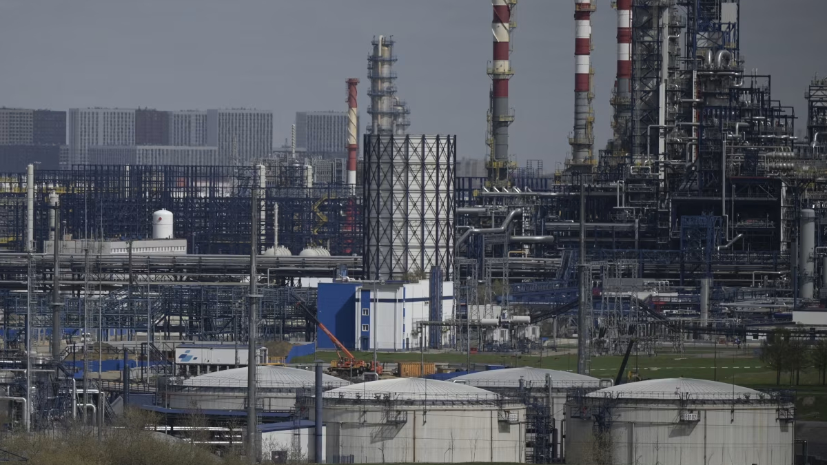 Extensive chemical refinery complex with storage tanks, pipes, and tall red-and-white smokestacks.