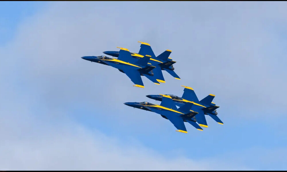 Two Blue Angels fighter jets flying in tight formation against a blue sky with light clouds.