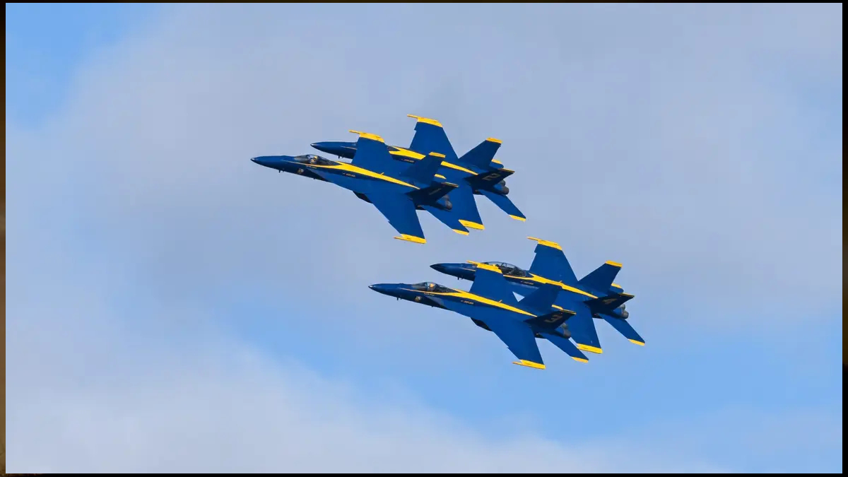 Two Blue Angels fighter jets flying in tight formation against a blue sky with light clouds.