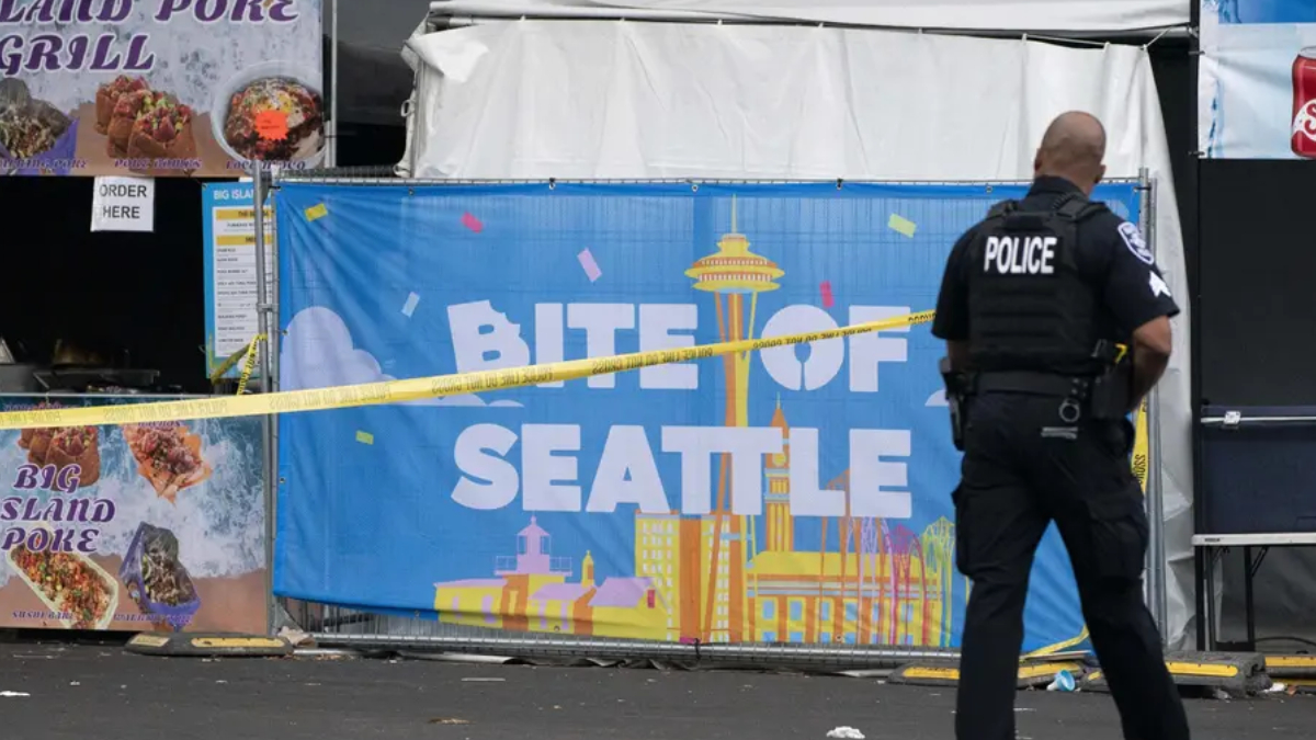 Police officer with back to camera guards a food festival booth; a blue banner reads 'BITE OF SEATTLE' with skyline illustrations and yellow caution tape across the scene.