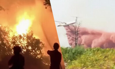 Silhouetted figures watch a large wildfire with intense flames on the left, and a helicopter near smoke on the right.