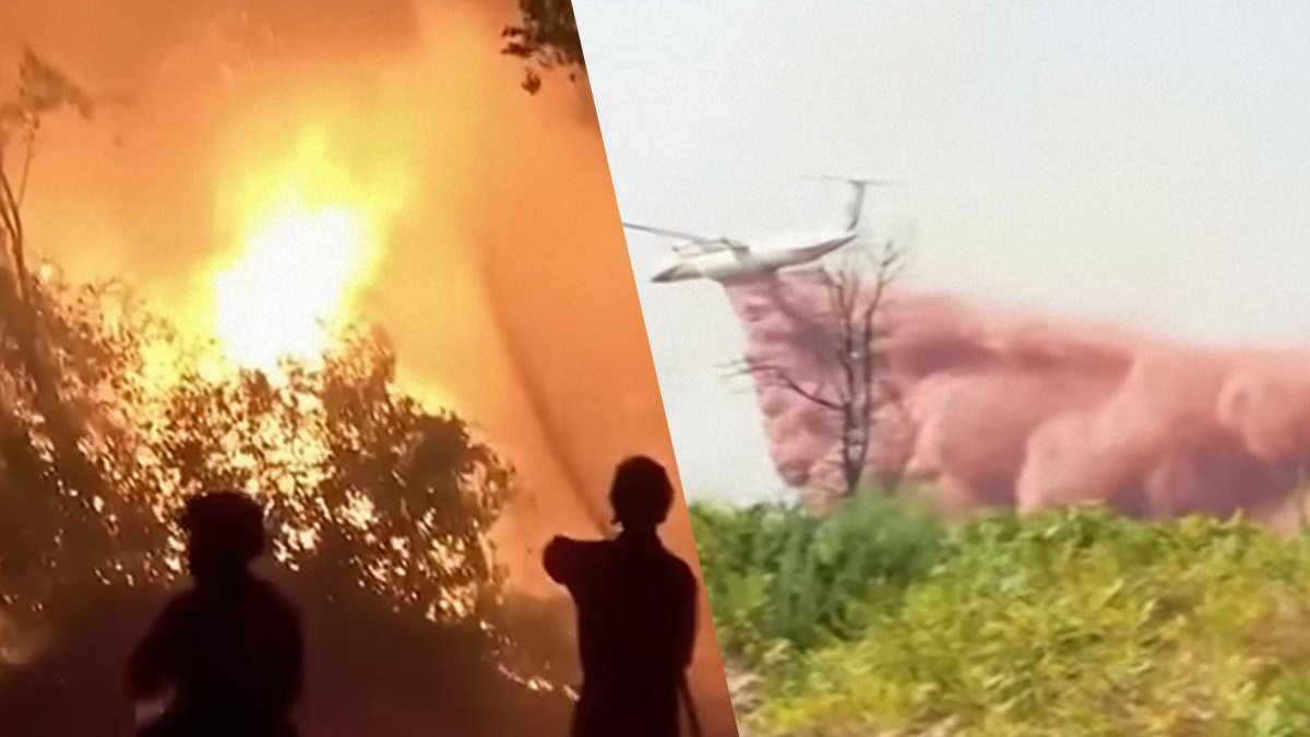 Silhouetted figures watch a large wildfire with intense flames on the left, and a helicopter near smoke on the right.