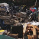 Chaotic outdoor junk pile with bikes, wood, bricks, and scattered debris in a cluttered yard.