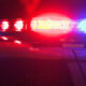 Police car with red and blue emergency lights flashing at night, reflecting off the car’s surface.