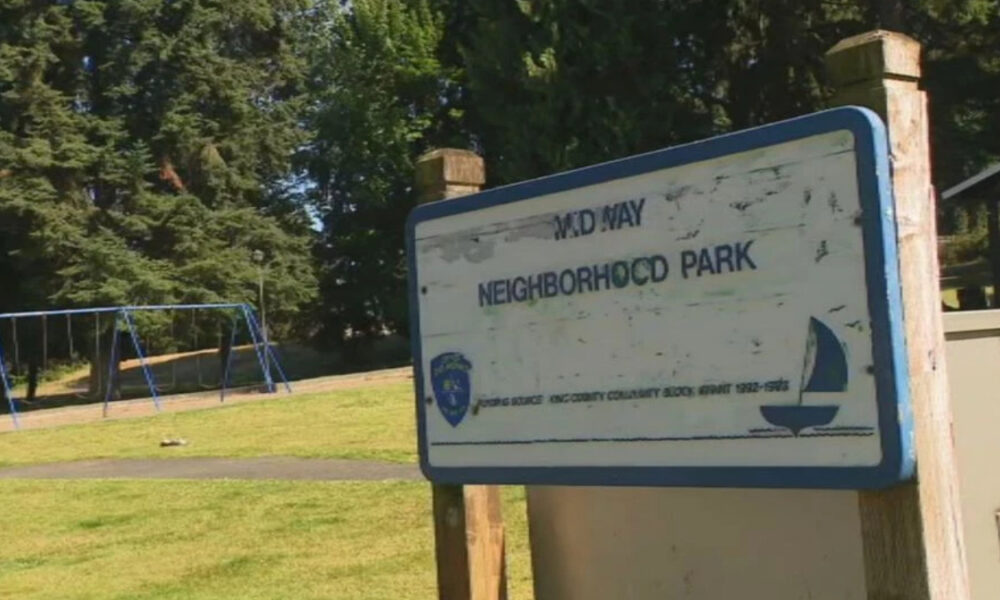 Sign for MD Way Neighborhood Park with a playground in the background (blue swings) in a grassy park area.