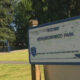 Sign for MD Way Neighborhood Park with a playground in the background (blue swings) in a grassy park area.