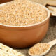Bowl of bulgur wheat in a ceramic dish with a wooden spoon and wheat stalks on burlap fabric (rustic setting)