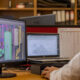 Engineer at a desk editing a 3D CAD model of a mechanical piping system on a monitor without cluttered background