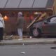 Car crashed into a storefront, glass shattered and debris on the sidewalk, bystanders nearby inspecting the scene