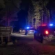 Police cars with flashing red and blue lights on a forest road at night, near a sign for Tinkham Road Forest Camp in Mt. Baker–Snoqualmie National Forest.