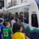 Crowded platform with soccer fans in colorful jerseys near a white-and-blue light-rail train at Seattle station.