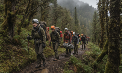 Group of hikers wearing helmets and backpacks trekking along a muddy forest trail in misty woods.
