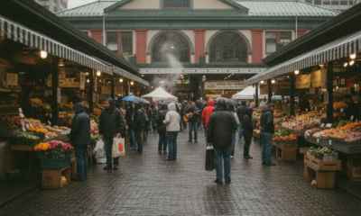 Bustling outdoor market with stalls of fruits and vegetables and shoppers in jackets on a wet cobblestone street.