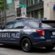 Seattle Police Department SUV parked on a city street with buildings and green trees in the background, text 'SEATTLE POLICE' visible on the side side of the vehicle