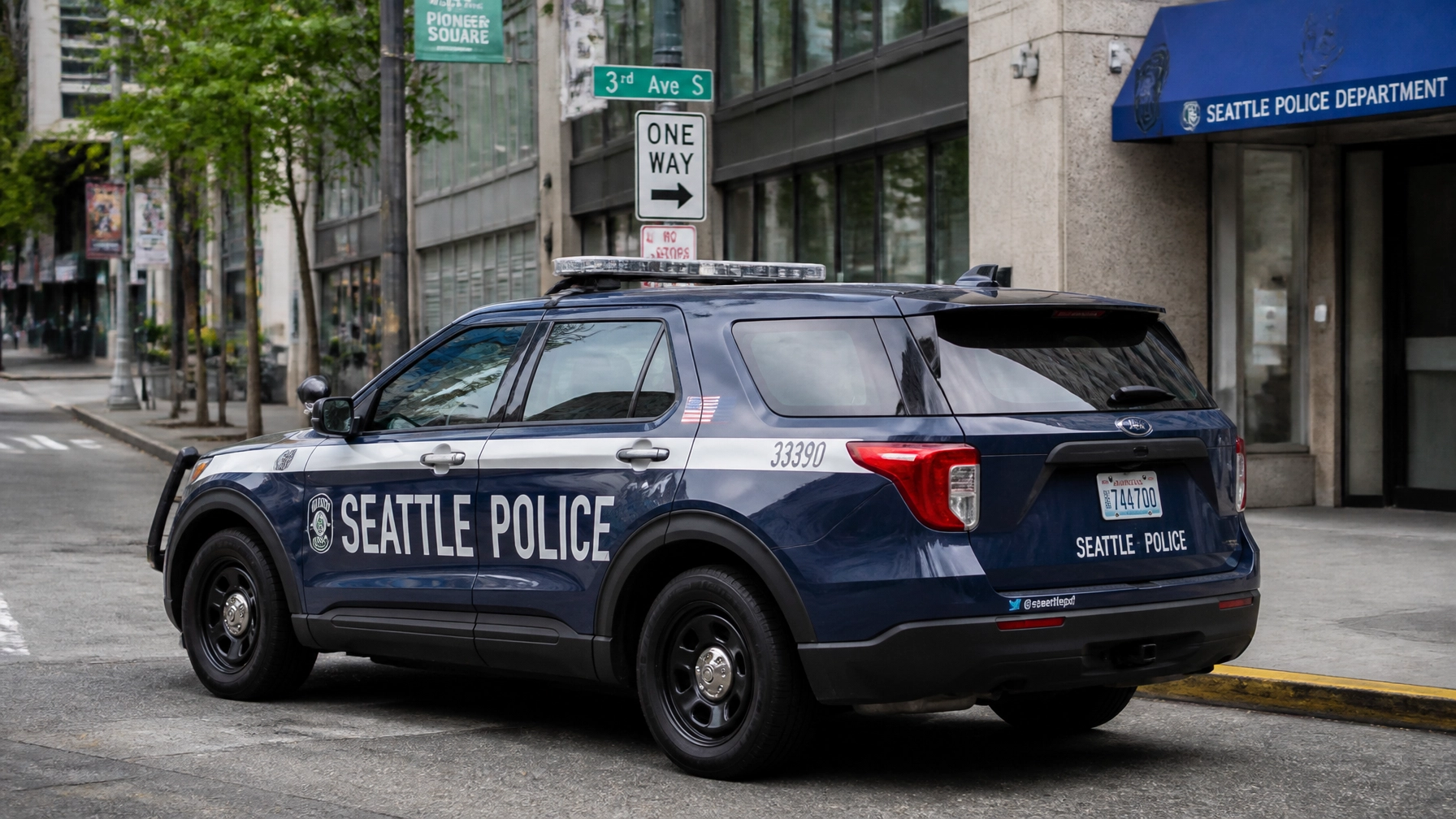 Seattle Police Department SUV parked on a city street with buildings and green trees in the background, text 'SEATTLE POLICE' visible on the side side of the vehicle