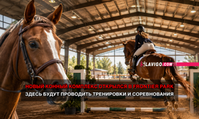 Indoor riding arena with a rider jumping a horse over a obstacle; foreground horse gazes toward the camera; overlaid red-and-white Russian text announces the new equestrian complex opening at Frontier Park and that trainings and competitions will be held there.