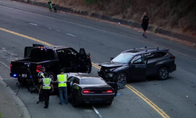Accident scene with two damaged SUVs on a two-lane road; police and investigators in reflective vests inspect the vehicles amid scattered debris.