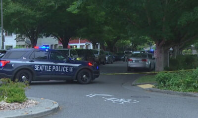 Seattle Police SUV blocks a tree-lined residential street with flashing lights and yellow tape across the road.