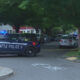 Seattle Police SUV blocks a tree-lined residential street with flashing lights and yellow tape across the road.