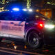 Bellevue Police SUV with flashing blue lights at night on a city street with holiday lights in the background.