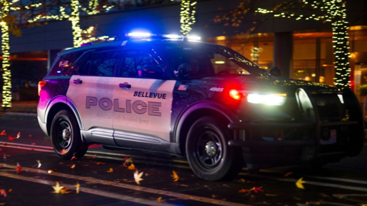 Bellevue Police SUV with flashing blue lights at night on a city street with holiday lights in the background.