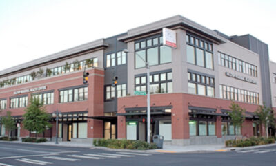 Corner view of a modern multi‑story medical and retail building with brick and gray siding on a city street.