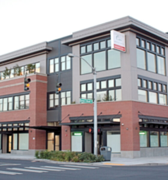 Corner view of a modern multi‑story medical and retail building with brick and gray siding on a city street.