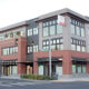 Corner view of a modern multi‑story medical and retail building with brick and gray siding on a city street.