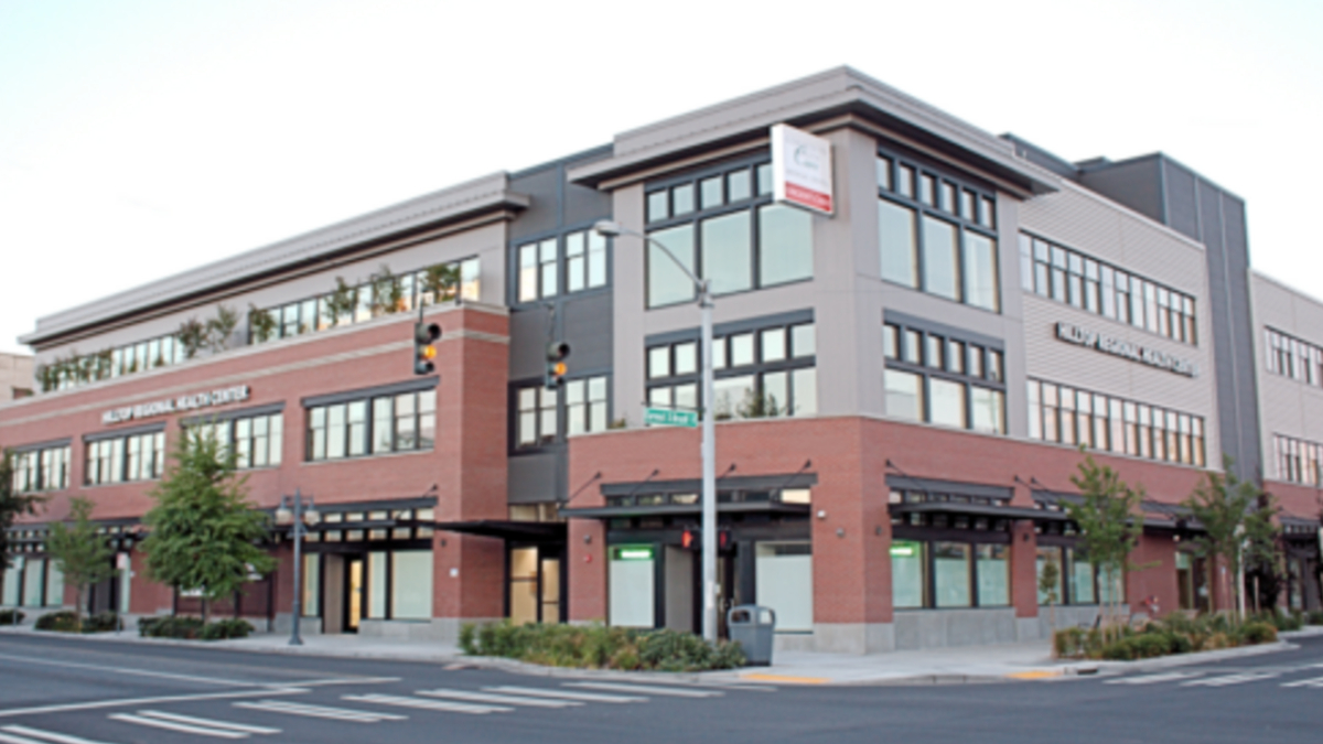 Corner view of a modern multi‑story medical and retail building with brick and gray siding on a city street.