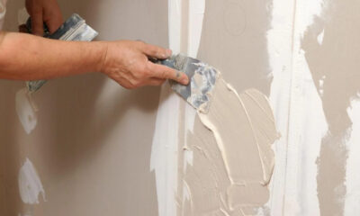 Worker smoothing beige plaster onto a wall with a putty knife during renovation