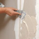 Worker smoothing beige plaster onto a wall with a putty knife during renovation