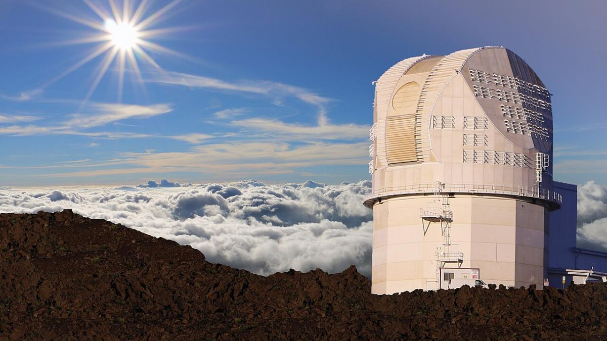 Observatory dome on a rocky mountaintop above the clouds with a bright sun in a clear blue sky.