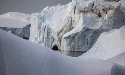 Snowy glacier landscape with blue-tinged ice cliffs and a meltwater pool nearby, calm and reflective.