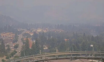Hazy panoramic view of a suburban city surrounded by trees, seen from a high overlook with a metal guardrail in the foreground.