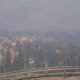 Hazy panoramic view of a suburban city surrounded by trees, seen from a high overlook with a metal guardrail in the foreground.