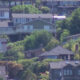 Hilly suburban neighborhood with closely spaced houses and green trees across the slope.