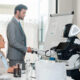 Business meeting where a robot shakes hands with a man in a gray suit, as colleagues watch in a bright office.