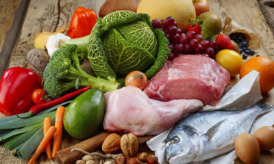 Assorted groceries on a wooden table: vegetables, fruits, poultry, fish, eggs, and nuts mix.