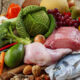 Assorted groceries on a wooden table: vegetables, fruits, poultry, fish, eggs, and nuts mix.