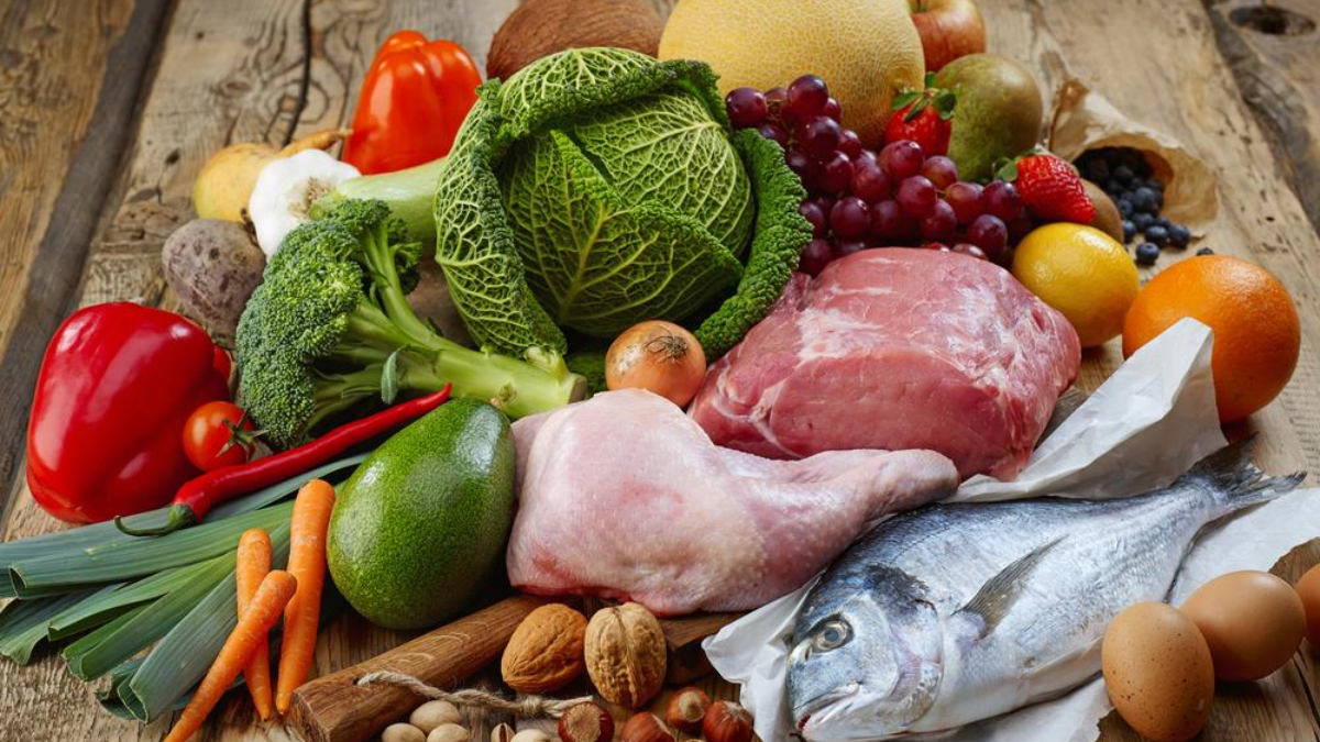 Assorted groceries on a wooden table: vegetables, fruits, poultry, fish, eggs, and nuts mix.