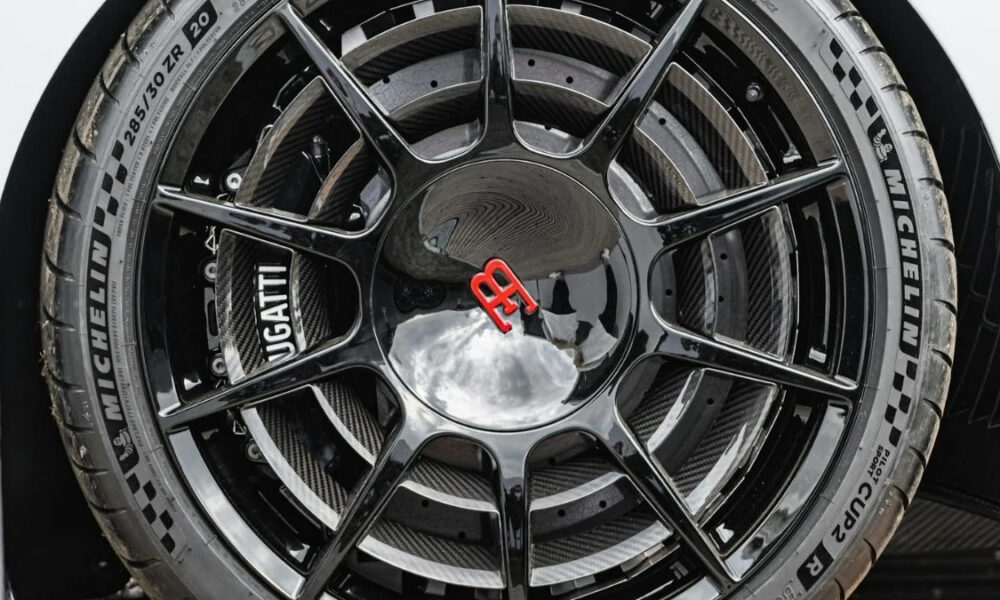 Close-up of a black multi-spoke alloy wheel with a red Bugatti emblem center cap and a Michelin tire visible surrounding it.