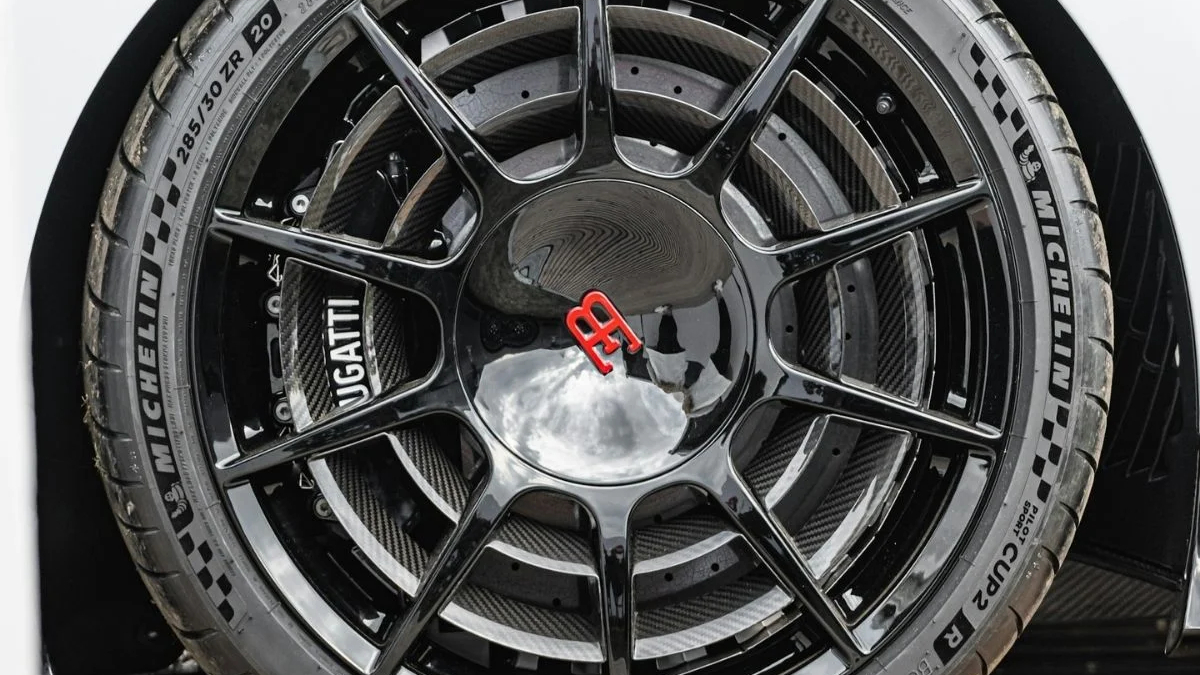 Close-up of a black multi-spoke alloy wheel with a red Bugatti emblem center cap and a Michelin tire visible surrounding it.