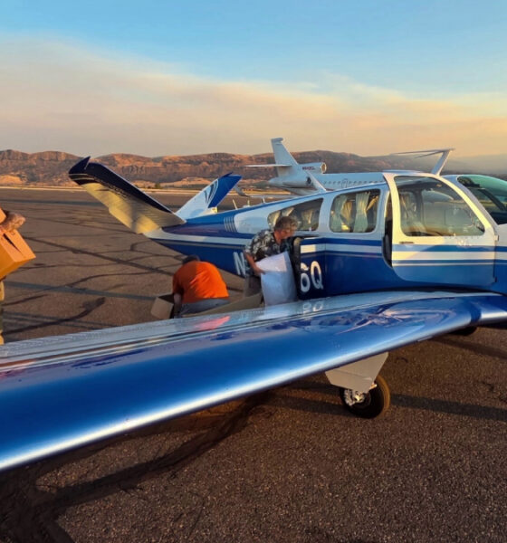 Blue single-engine plane on a sunlit runway with cargo doors open as workers load boxes at sunset.