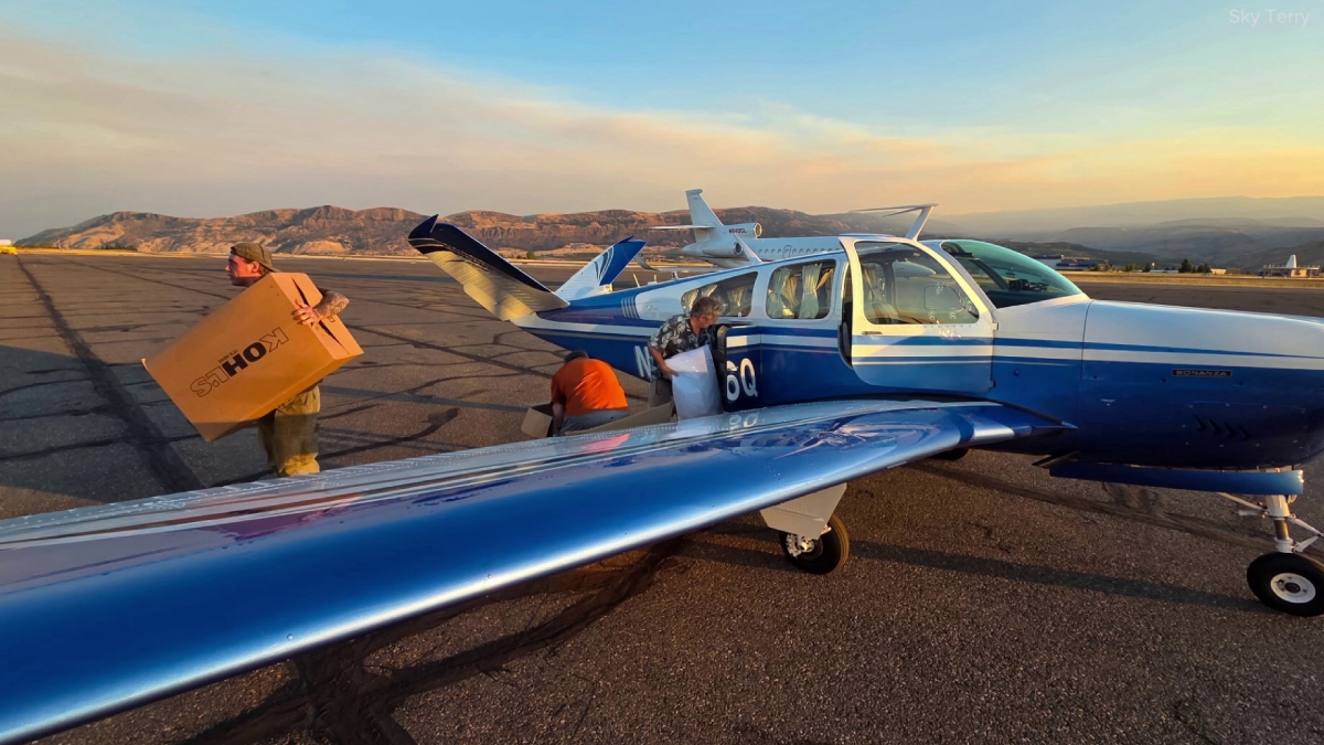 Blue single-engine plane on a sunlit runway with cargo doors open as workers load boxes at sunset.