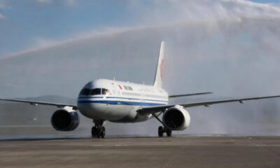 White commercial airliner with a blue stripe on a runway; water spray trails behind as it lands on a wet tarmac.